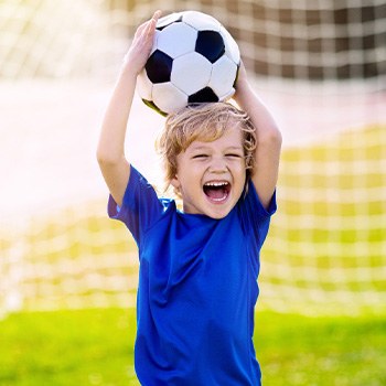 Child smiling while holding soccer ball on field